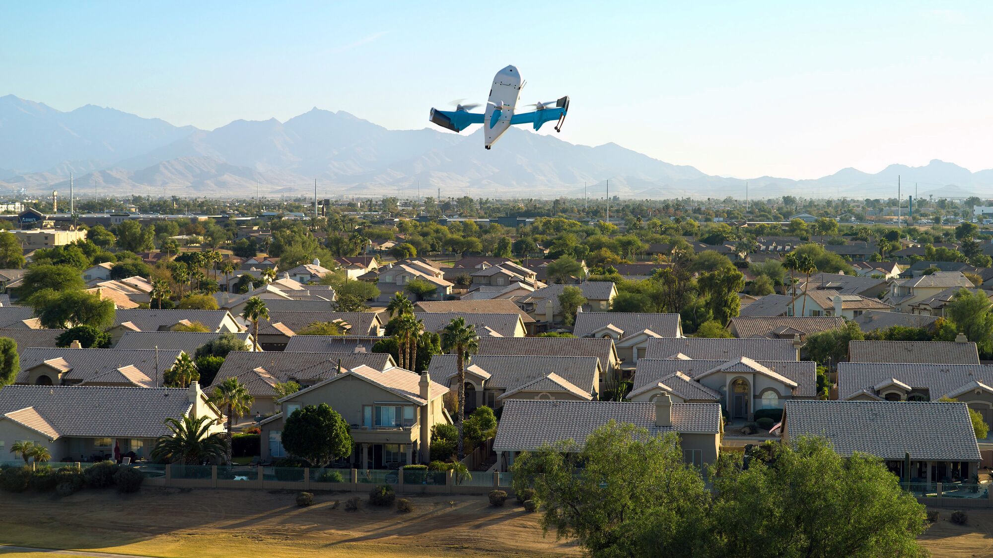 Drone flying over suburban neighborhood with mountains in background.